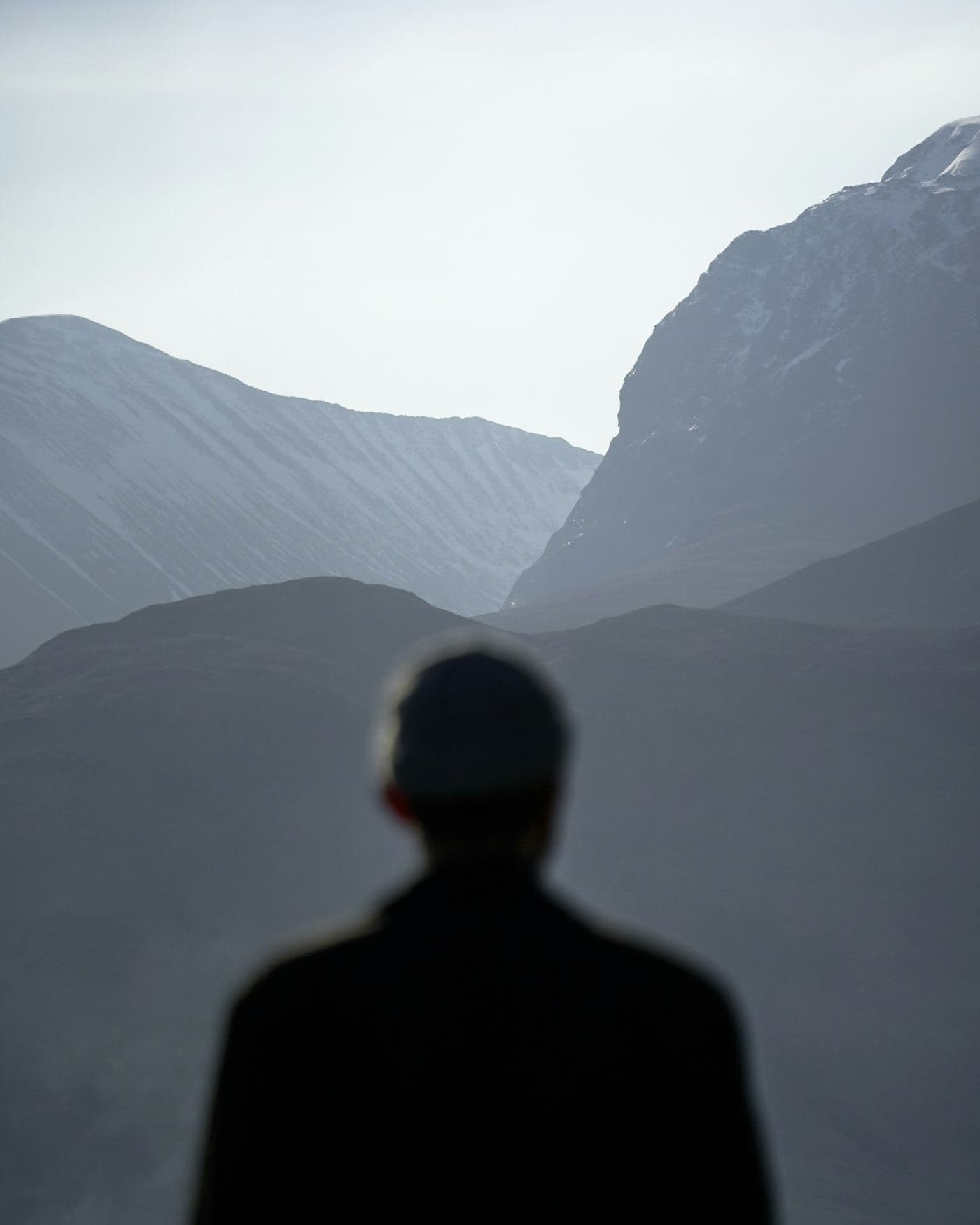 A man seen from behind, out of focus, facing a quiet mountain valley